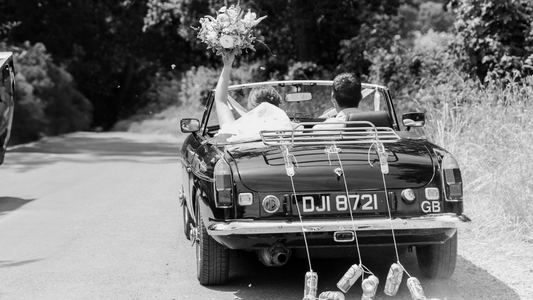 Black and white photograph of Daisy and her husband leaving their wedding in a classic car