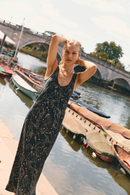 Woman wearing a black midi silk slip dress with gold print, featuring a scoop neckline and straps.