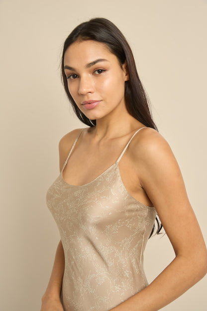 Woman wearing beige silk slip dress with scoop neckline and narrow straps.