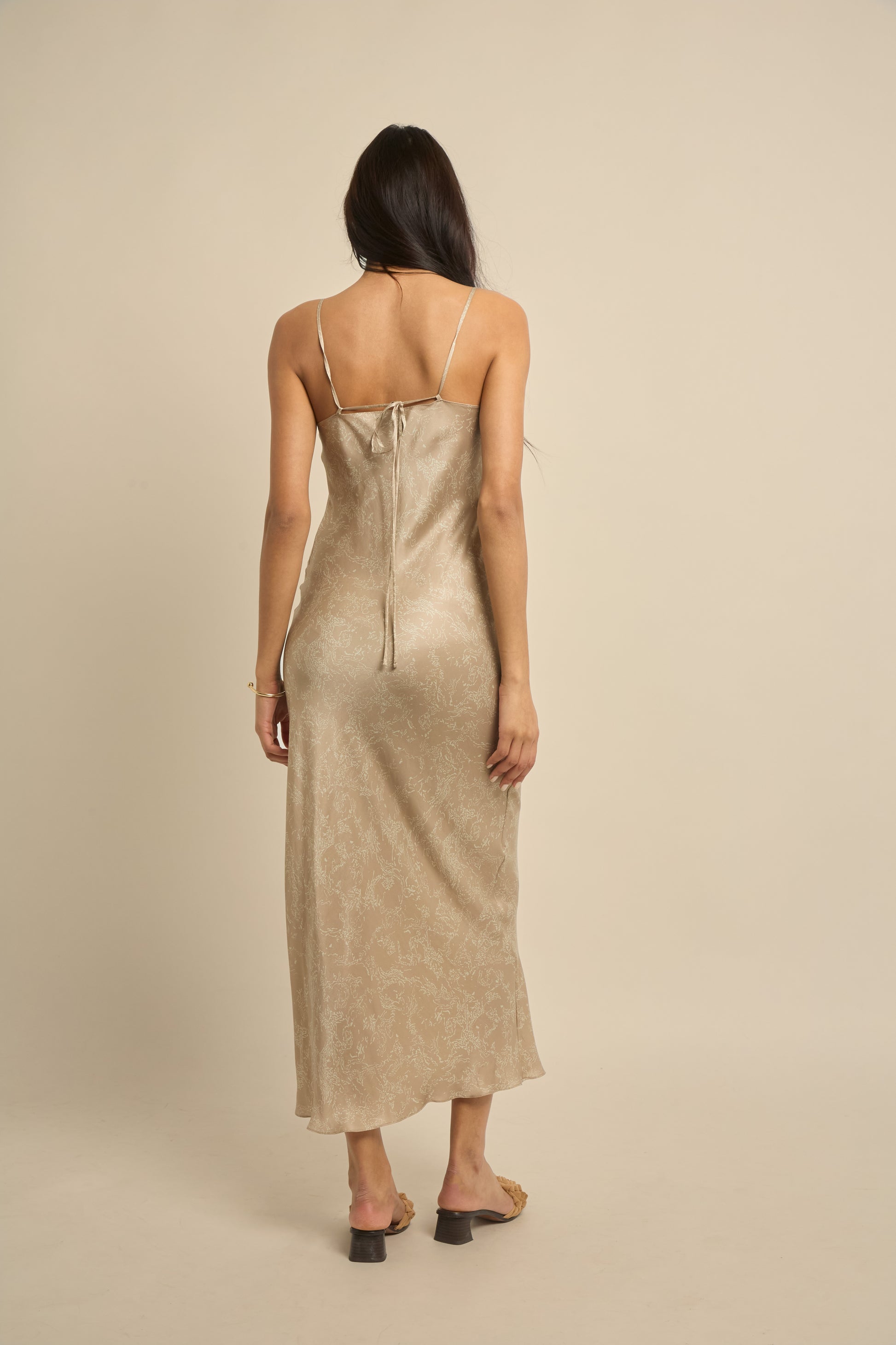 Woman wearing beige silk slip dress featuring a midi length and adjustable spaghetti straps. 